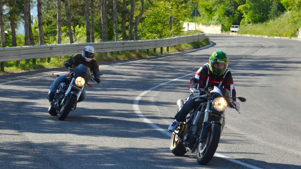 Két motoros kanyarodik a napfényes úton, élvezve a sebességet.