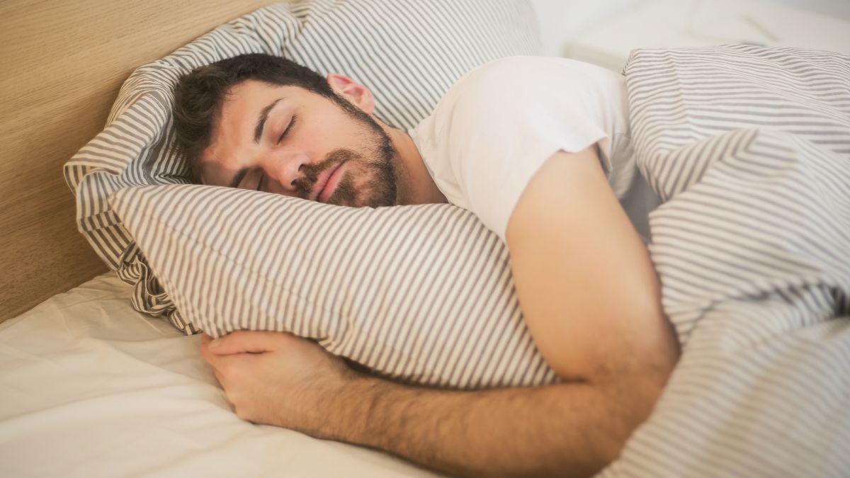 Egy férfi békésen alszik az ágyában, párnára hajtott fejjel.