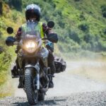 Motorkerékpáros terepen, porfelhőt kavarva halad a végsebesség-teszt során.