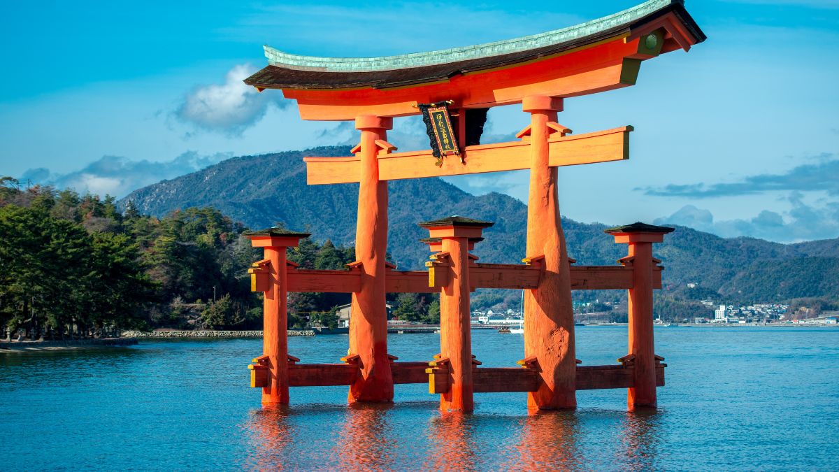 Egy gyönyörű torii kapu áll a vízben, háttérben hegyekkel Japánban.